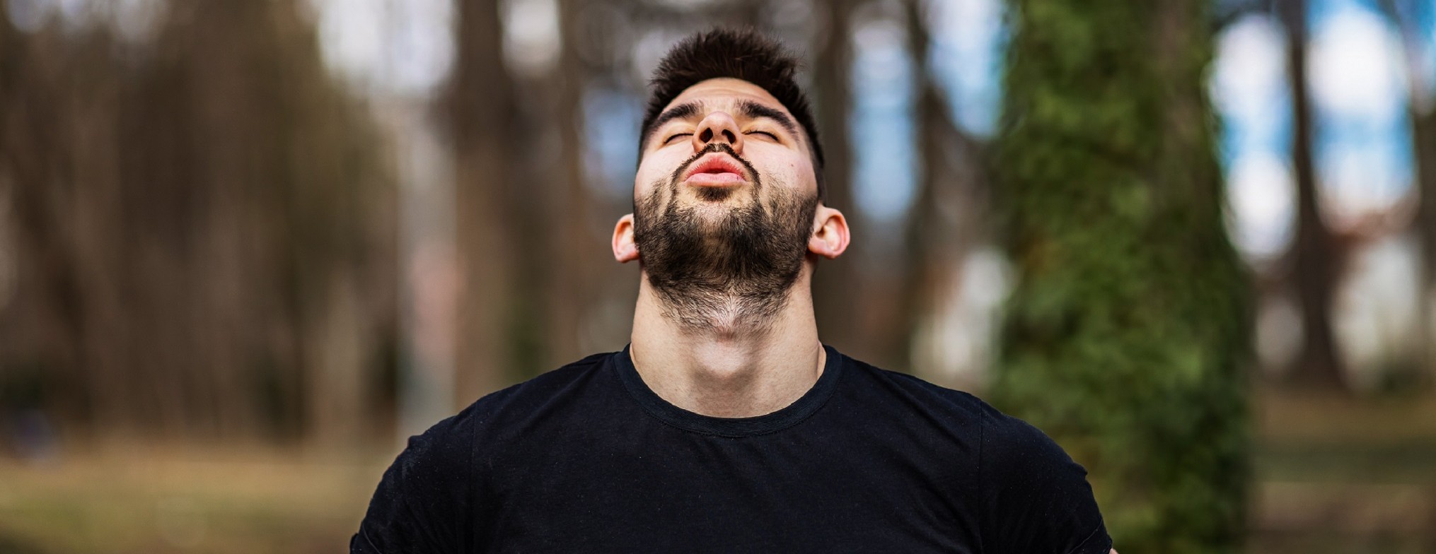 Man breathing in forest with head back and eyes closed