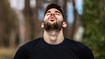 Man breathing in forest with head back and eyes closed